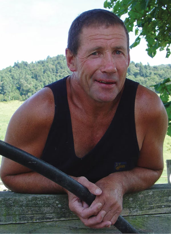 Man holding a black pole outdoors with greenery in the background