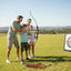 Family practicing archery in a field with a target in the background