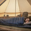 Person lying in a sleeping bag inside a tent with camping gear around