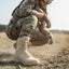 Person in military uniform and boots crouching in a field