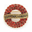 A circular remembrance pin featuring a wreath of red poppies with gold-tone outlines and a central gold banner inscribed with 'LEST WE FORGET'.