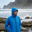 Person wearing a blue jacket standing on a rocky beach with ocean and cliffs in the background