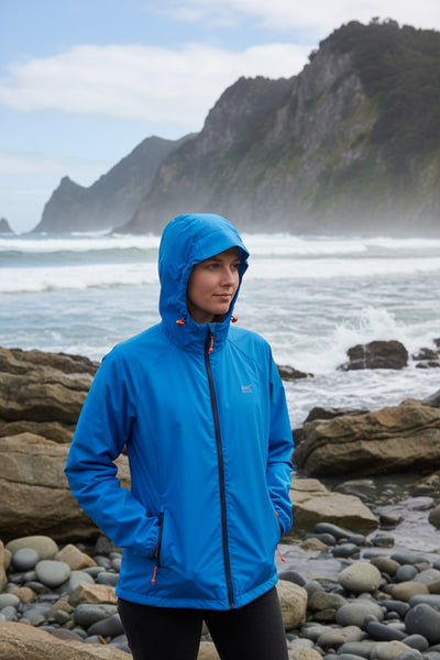 Person wearing a blue jacket standing on a rocky beach with ocean and cliffs in the background