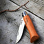 Orange folding knife with silver blade on a wooden surface
