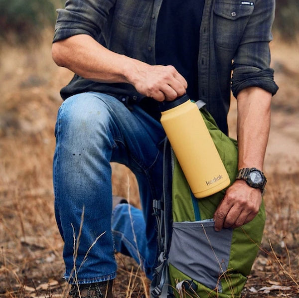 Person holding a yellow water bottle with a green backpack outdoors
