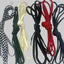 Four coiled rope or cord bundles in different colors and patterns, including black-and-white checkered, dark green, cream, and red, arranged side by side on a plain light gray background.