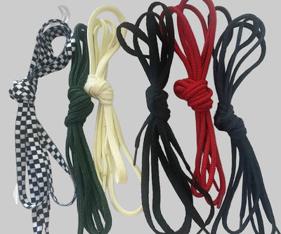 Four coiled rope or cord bundles in different colors and patterns, including black-and-white checkered, dark green, cream, and red, arranged side by side on a plain light gray background.