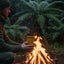 Person holding a yellow mug over a campfire in a forest setting