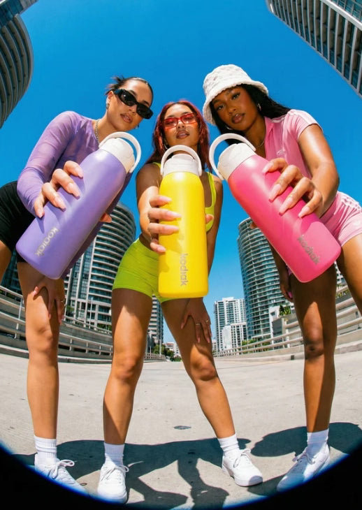 Three women holding colorful water bottles against a cityscape background