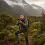 Man in camouflage gear holding a rifle in a mountainous forest
