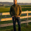 Man standing in a field with a wooden fence and green landscape in the background
