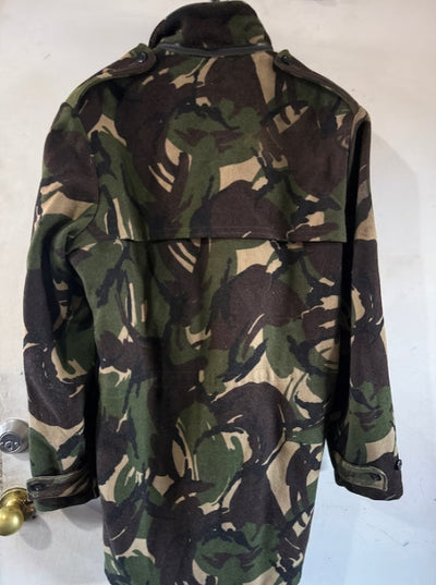 A military-style camouflage jacket with a high collar and shoulder epaulets, shown from the back against a plain off-white wall.
