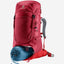A red Deuter hiking backpack shown on a light gray background, with a blue sleeping bag tucked underneath. The backpack features multiple zippered compartments, side compression straps, and a gray padded shoulder strap.