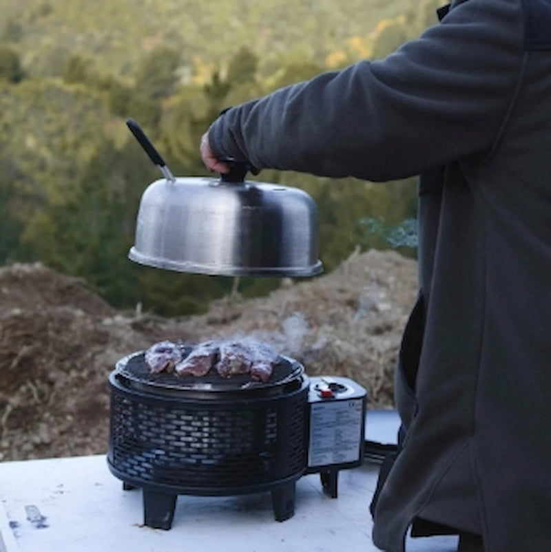 Person cooking on a portable grill outdoors with a scenic background