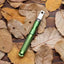A green fire starter with a metallic rod and a loop on one end, placed on a bed of brown leaves.