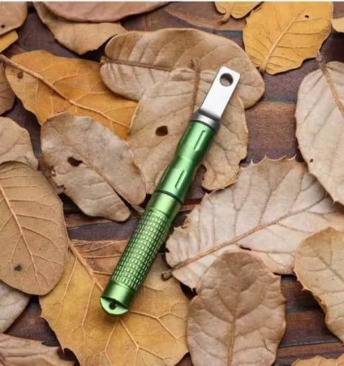 A green fire starter with a metallic rod and a loop on one end, placed on a bed of brown leaves.