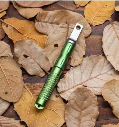 A green fire starter with a metallic rod and a loop on one end, placed on a bed of brown leaves.