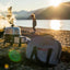 Person by a lake with a backpack and portable stove at sunset