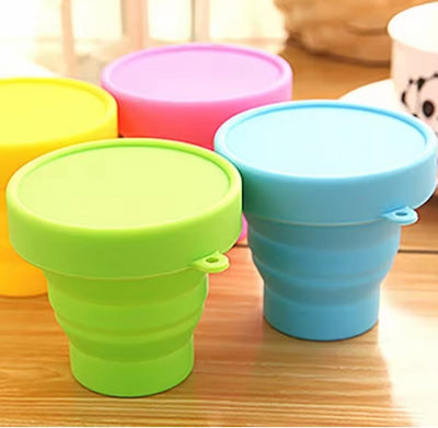 Collapsible silicone cups in green, blue, and pink on a wooden surface.
