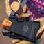 Black tool with orange clip held by a gloved hand, blurred colorful background