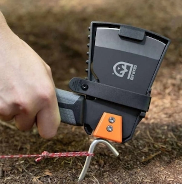 Person using a black and orange tool with a brand logo on a dirt background