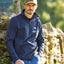 Man wearing a navy fleece pullover with a logo, standing outdoors near a stone wall.
