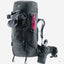 A dark gray Deuter hiking backpack with multiple compartments, shown with a pink trekking pole tucked into a side pocket and a water bottle in a side pouch, on a light gray background.