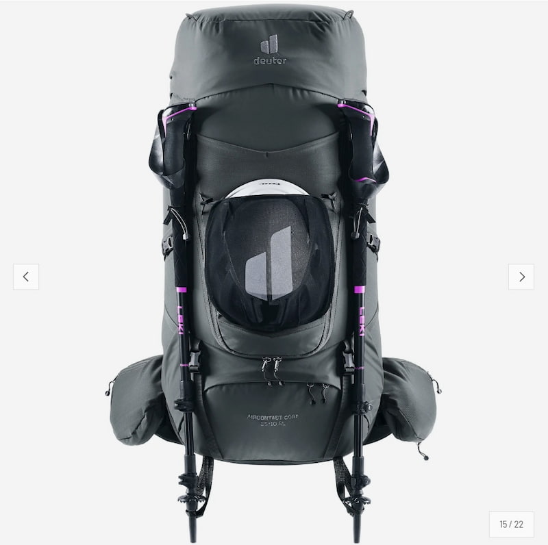 A dark gray Deuter hiking backpack shown from the front, featuring a large front mesh pocket, side compression straps, and two black trekking poles attached. The backpack has purple accent details and a white Deuter logo on the top panel.