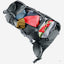 A dark gray outdoor backpack shown open, filled with camping gear including a red sleeping bag, a tan pouch, and other gear, on a light gray background.
