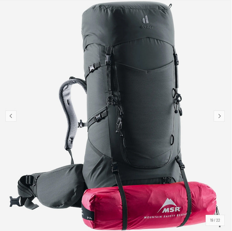 A dark gray Deuter hiking backpack with multiple compartments, shown with a pink trekking pole tucked into a side pocket and a water bottle in a side pouch, on a light gray background.