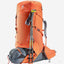 An orange and gray hiking backpack shown on a light gray background, with a gray sleeping bag rolled at the base and two trekking poles leaning against the front. The backpack has the Deerrun brand logo visible near the top left.