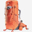 An orange Deuter hiking backpack shown on a light gray background, with a matching orange hydration bottle and a gray neck gaiter.