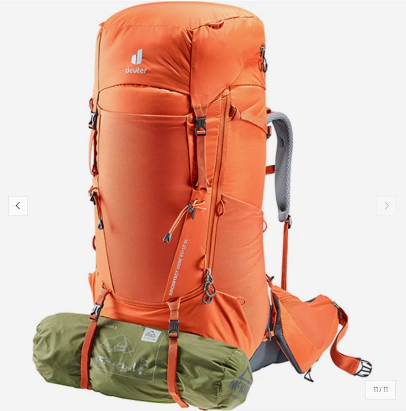 An orange Deuter hiking backpack shown on a light gray background, with a green sleeping bag or gear roll strapped to the bottom and a gray shoulder strap visible on the side.