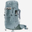 A Deuter hiking backpack in a muted slate blue-gray color, shown from a three-quarters angle against a light gray background. The backpack features multiple zippered compartments, a side water bottle pocket holding a silver bottle, and padded shoulder straps.