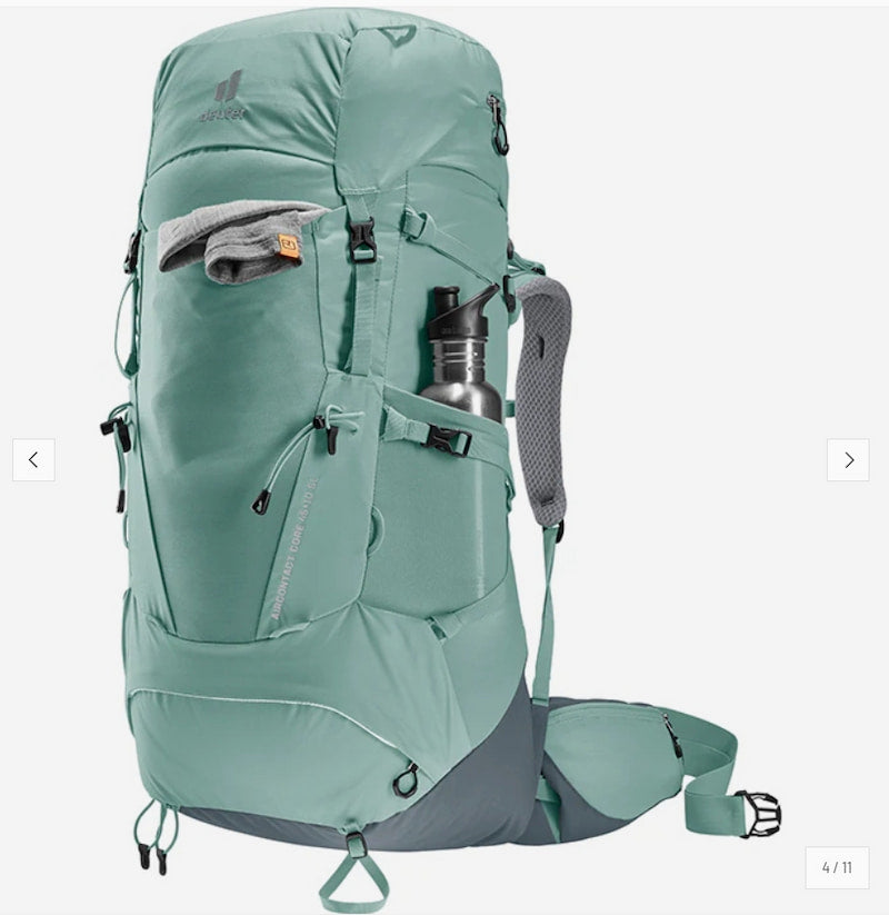 A large hiking backpack in a muted sage green color, shown from a three-quarter angle on a light gray background. The backpack features multiple zippered compartments, a side water bottle pocket holding a silver water bottle, and gray padded shoulder straps.