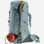 A Deuter hiking backpack in slate blue-gray, shown with two hiking poles and a red sleeping bag pouch against a light gray background.