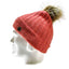 A ribbed knit beanie in a muted coral pink color, featuring a brown faux-fur pom-pom and a small black button on the side, displayed on a white mannequin head against a white background.
