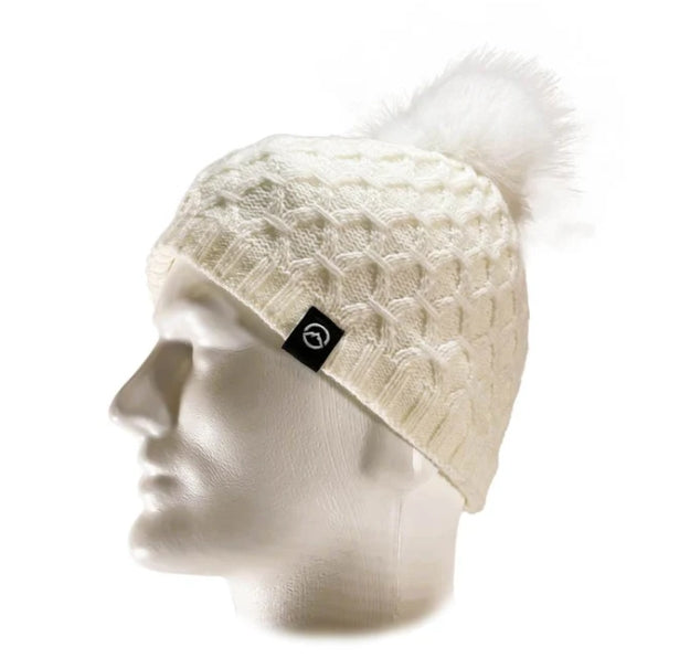 An off-white cable-knit beanie hat with a fluffy pom-pom on top, displayed on a white mannequin head. A small black square tag with a white circular logo is attached to the side of the hat.