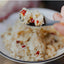Close-up of a spoonful of rice with red peppers over a plate of rice.