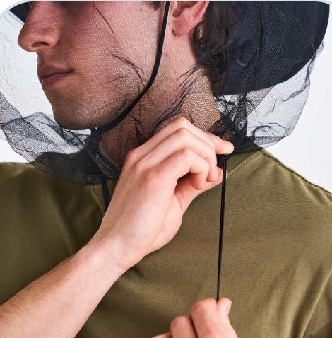 Person wearing a green shirt with a black insect netting over their head against a white background