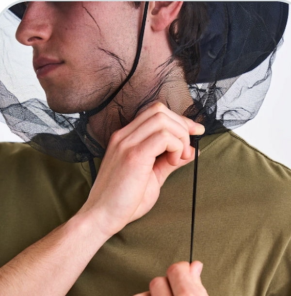 Person wearing a green shirt with a black insect netting over their head against a white background