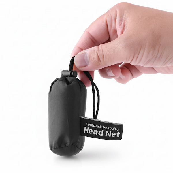 Hand holding a black compact mosquito head net with a visible brand label on a white background