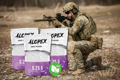 A soldier in camouflage kneels outdoors holding a rifle, with three bags of ALOPEX Airsoft Precision pellets in the foreground. The bags are white and purple with the ALOPEX brand name and '0.