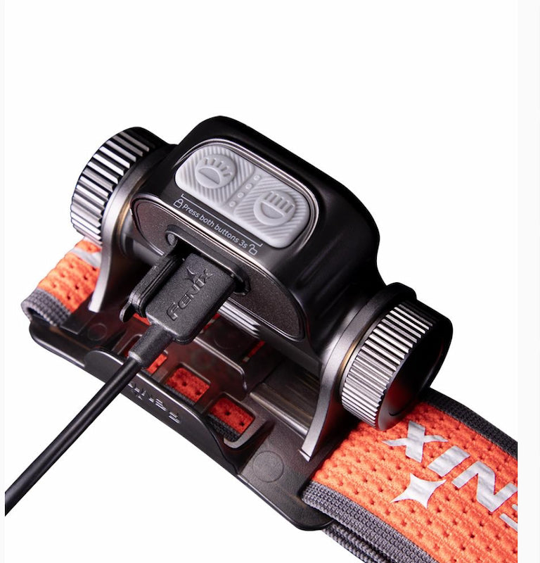 Close-up of a headlamp with orange strap and control buttons on a white background