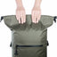 Person holding a green backpack with black zippers on a white background