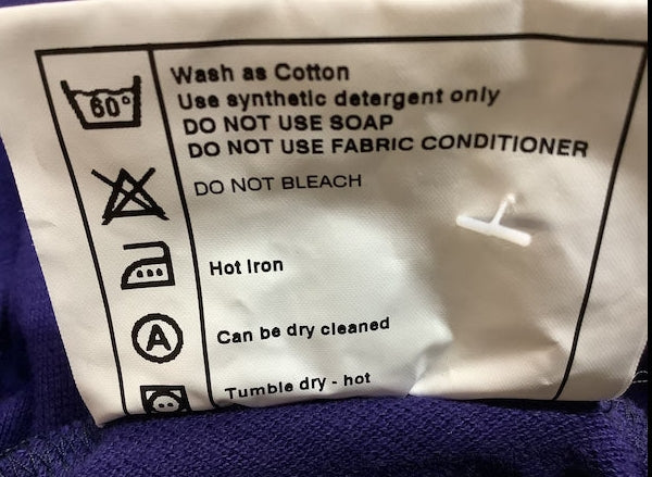 Close-up of a garment care label showing washing instructions, including 'Wash as Cotton', 'Use synthetic detergent only', 'DO NOT USE SOAP', 'DO NOT BLEACH', and 'Hot Iron'.