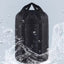 A black sleeping bag compression sack with a pull cord top, depicted with water splashing around it to illustrate its waterproof feature.