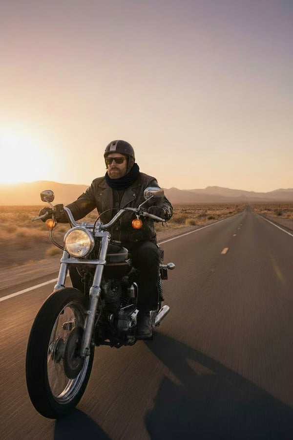 Person riding a motorcycle on a desert road at sunset