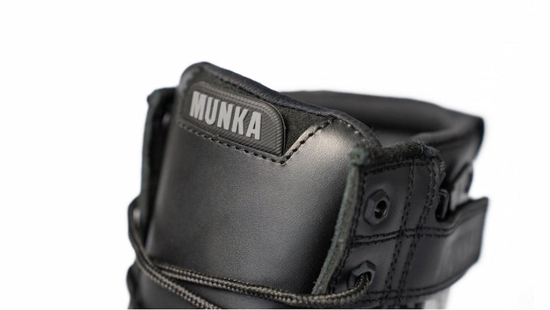 Close-up of a black Munka hockey shin guard showing the padded collar with the brand name 'MUNKA' in white on a black tab, set against a plain white background.