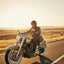 Man riding a motorcycle on a desert road with a sunset in the background